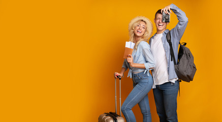 Young couple posing with tickets and camera over yellow background