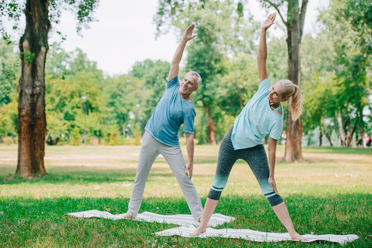 smiling, mature man and woman standing in warrior poses while practicing yoga in park