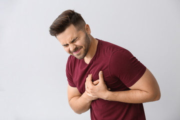 Young man suffering from heart attack on light background