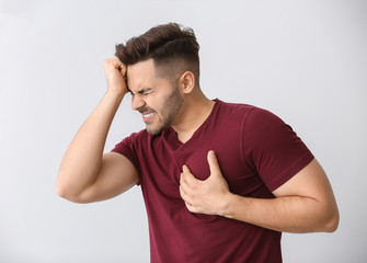 Young man suffering from heart attack on light background