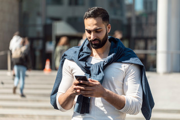 Businessman looking at his mobile phone while walking on street to office