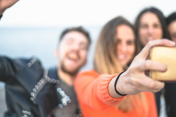 Defocused, unrecognizable young people, having fun taking a selfie outdoors at the seaside. Focus on the hand holding the smartphone