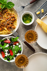 Large plate of spaghetti with bolognese sauce, slat and glasses with white wine on a gray background top view