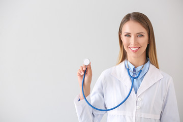 Female doctor with stethoscope on light background