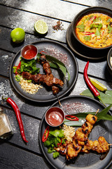 Asian dishes on a black table. Satay and Tom Yam