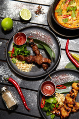 Asian dishes on a black table. Satay and Tom Yam