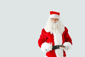 Portrait of Santa Claus with milk and cookies on light background