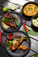 Asian dishes on a black table. Satay and Tom Yam
