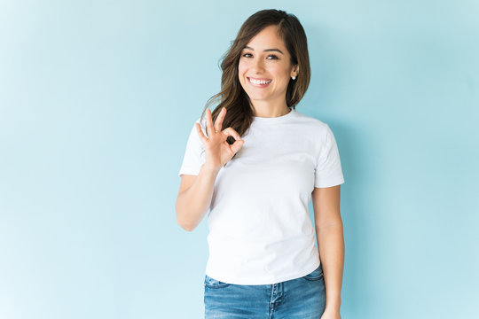 Brunette Woman Making OK Hand Sign Over Blue Background