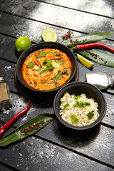 Asian dish on a black plate. Tom yum with rice