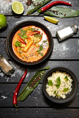 Asian dish on a black plate. Tom yum with rice