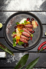 Asian dish on a black plate. Duck breast with peach