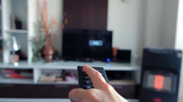 Close-up of female hand using TV remote control and switching channels on television.