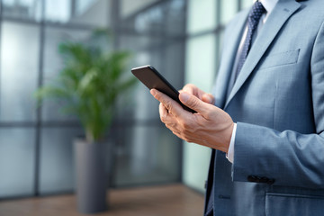 Close up of businessman wearing grey suit holding black smartphone