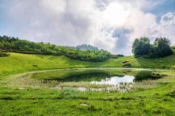 View of a mountain lake with clear water and reflection at cloudy summer day.