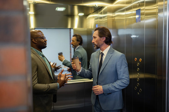 Grey-haired man talking to colleague while standing in elevator