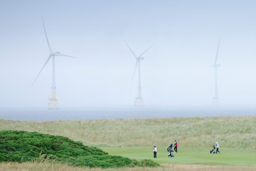 Fototapeta na wymiar Donald Trump golf course showing wind farm turbines and golfers in the North Sea