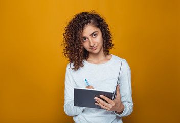 Portrait of a beautiful Indian girl writing on a notepad. Muslim young woman of mixed race on an orange background in the studio. 