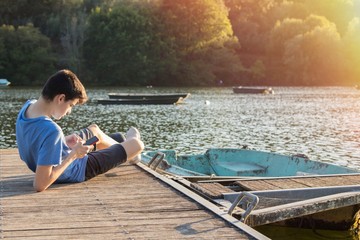 young man with mobile phone on the jetty at sunset