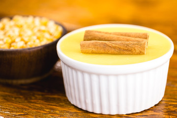 Brazilian sweet cream-like dessert cured corn mousse with cinnamon on a rustic wooden background. Typical Brazilian cuisine sweet in traditional parties, on a wooden background with copy space.