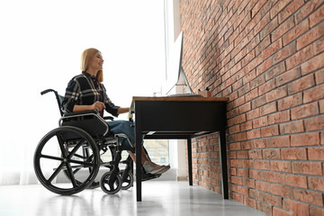 Woman in wheelchair working with computer at table indoors