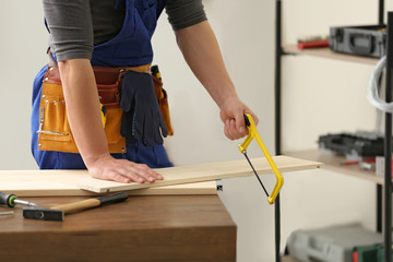 Young working man using hand saw indoors, closeup. Home repair