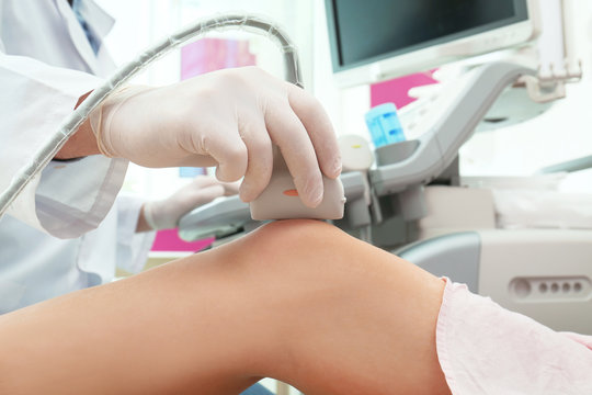 Doctor Conducting Ultrasound Examination Of Knee Joint In Clinic, Closeup