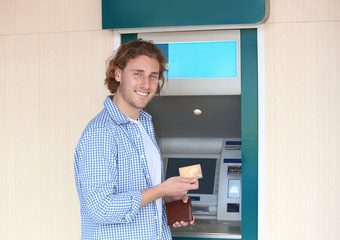 Young man with credit card near cash machine outdoors