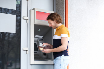 Fototapeta na wymiar Young man with money near cash machine outdoors. Space for text