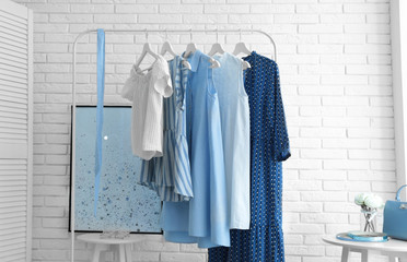 Wardrobe rack with women's clothes at white brick wall in room