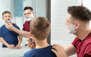 Obraz premium Dad applying shaving foam on son's face at mirror in bathroom
