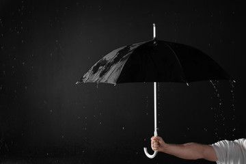 Man holding black umbrella under rain against dark background, closeup