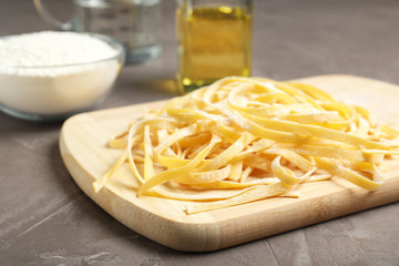 Board with uncooked egg noodles on grey table, closeup