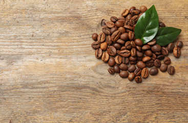 Pile of coffee beans and fresh green leaves on wooden table, top view with space for text