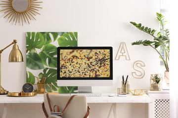 Modern workplace with computer and golden decor on desk near wall. Stylish interior design