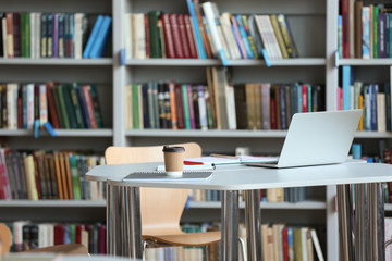 Laptop, drink and stationery on table in library