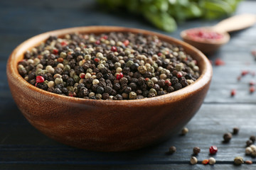Mix of peppercorns in bowl on dark wooden table, closeup