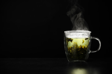 Glass cup of hot green tea on table against black background, space for text
