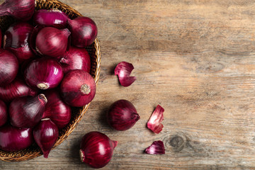 Wicker basket with red onions on wooden table, top view. Space for text