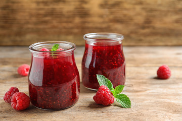 Glass jars of sweet jam with ripe raspberries and mint on wooden table. Space for text