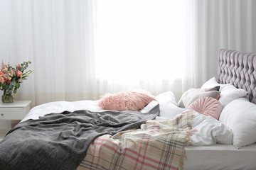 Comfortable bed with plaids and pillows in room