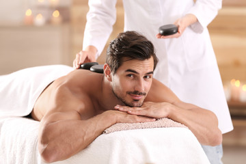 Fototapeta na wymiar Handsome young man receiving hot stone massage in spa salon