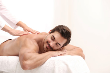 Handsome young man receiving back massage on light background, space for text. Spa salon