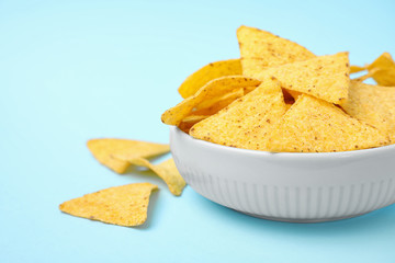Bowl with tasty Mexican nachos chips on light blue background, space for text