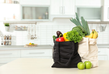 Textile shopping bags full of vegetables and fruits on table in kitchen. Space for text