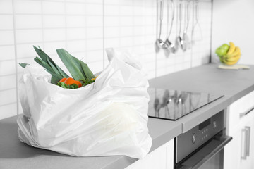 Plastic shopping bag full of vegetables on countertop in kitchen. Space for text