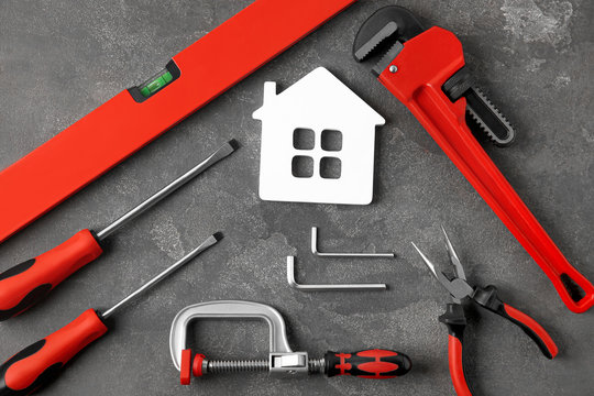 Set of repair tools and house figure on grey stone background, flat lay