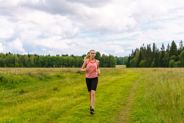 young woman jogging in the meadow and listening to music on headphones