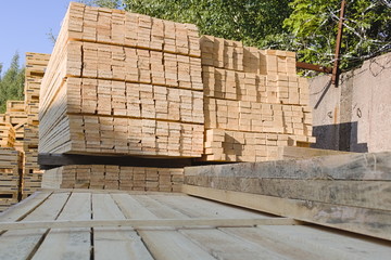 The boards are stacked in a warehouse in the open air in the summer. Industrial woodworking materials.