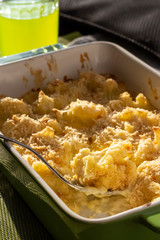 Cauliflower and cheese gratin in green ceramic baking form with fork. Bright natural light. Selective focus.